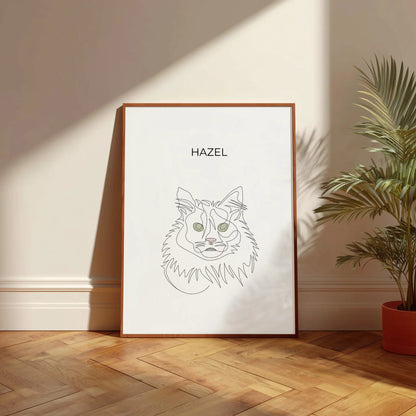 Minimalistisches One Line Art Katzenportrait mit Namen Hazel, individuelles Haustierportrait nach Fotovorlage im modernen Stil als Wandbild mit holzfarbenen Rahmen in 50x70cm vor einer hellen Wand neben einer Pflanze.